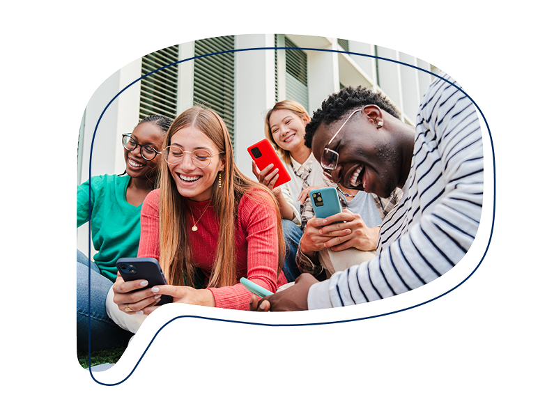 Vier junge Menschen sitzen zusammen im Freien und schauen lachend auf ihre Smartphones.